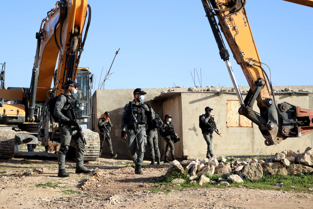 Israeli security forces stand guard while bulldozers prepare to destroy the house of Palestinian under the pretext of illegal construction in the West Bank city of Hebron on February 3, 2021. Israels maintains entrenched discriminatory systems that treat Palestinians unequally. Its over half-century-long occupation of the West Bank and Gaza involves systematic rights abuses, including collective punishment. It builds and supports illegal settlements in the occupied West Bank, expropriating Palestinian land and imposing burdens on Palestinians but not on settlers, restricting their access to basic services and making it nearly impossible for them to build in much of the West Bank without risking demolition. Photo by Mosab Shawer