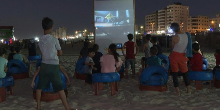 On a warm summer night, the sound of laughter and applause fills the air as a crowd of Palestinians watch a movie on a makeshift screen on the beach. They are enjoying a rare treat: a seaside cinema that offers them a brief escape from the hardships of life in the Gaza Strip.